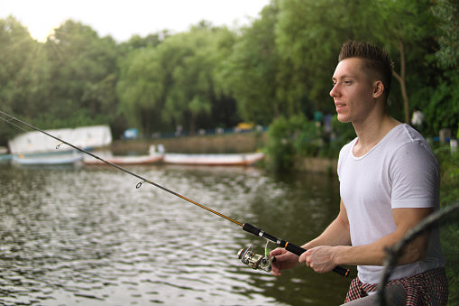 Man fishing on a serene lake with a dock in the background.