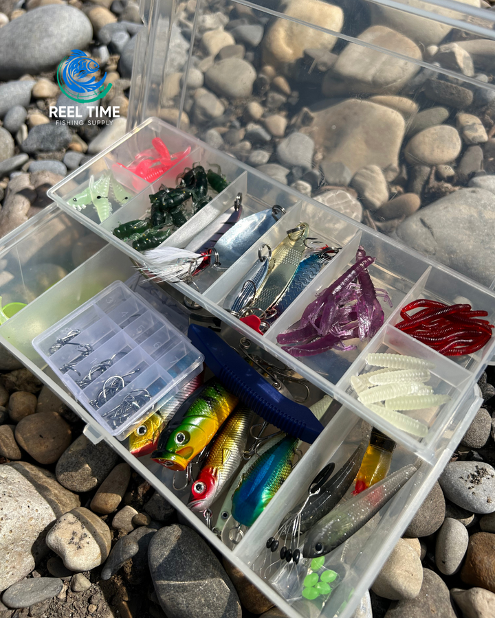 Close up angle of compact tackle box sitting on river rocks with lid open displaying included lures and tackle.