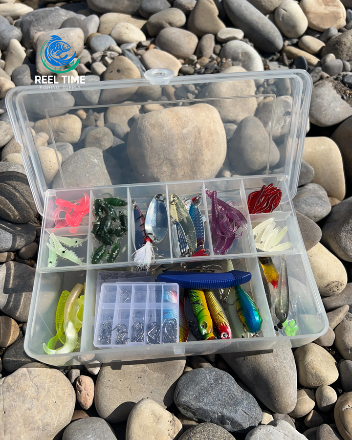 Compact tackle box sitting on river rocks with lid open displaying included lures and tackle.