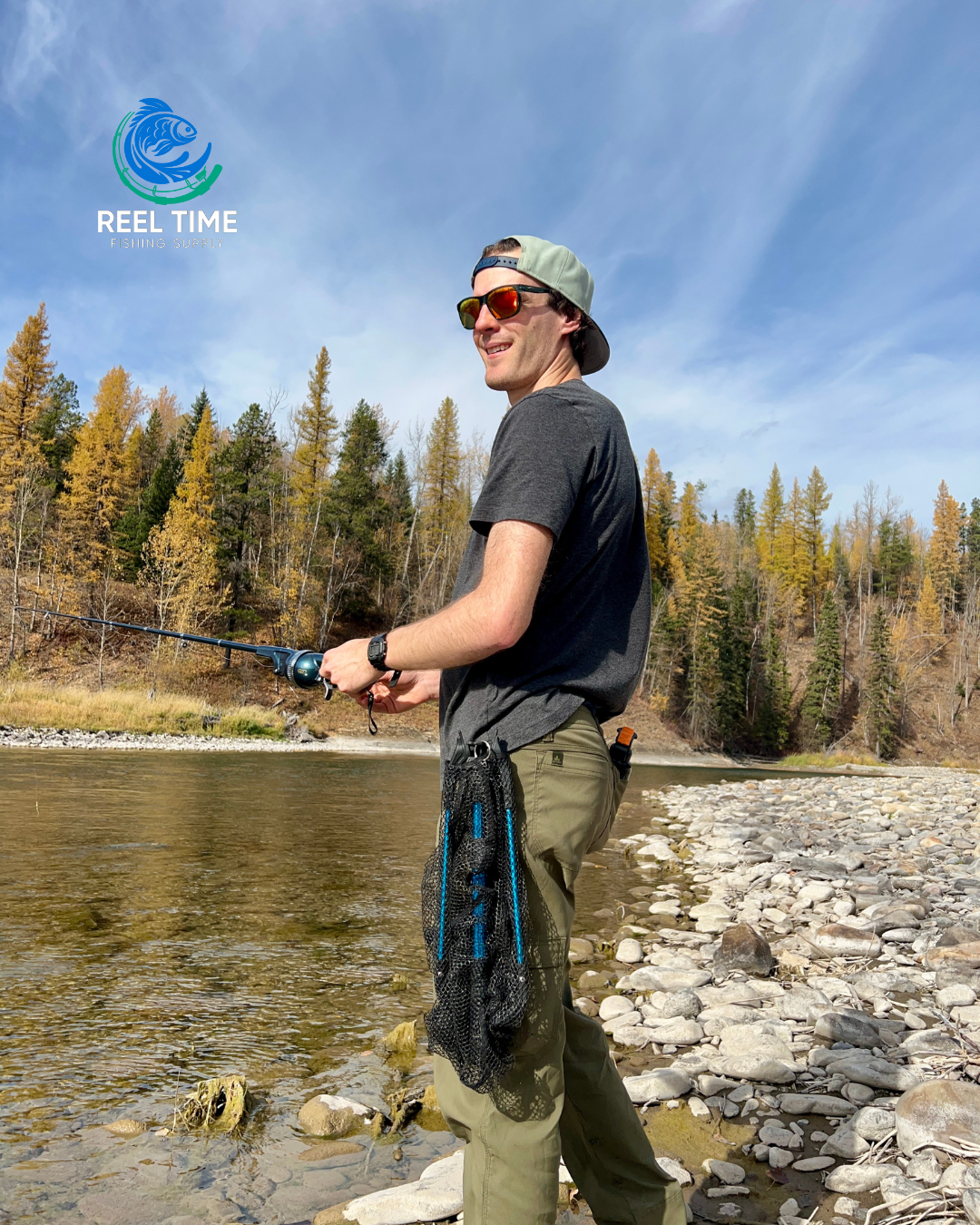 Angler standing by a river fishing. Collapsible landing net is clipped to his belt demonstrating its compact and portable design.